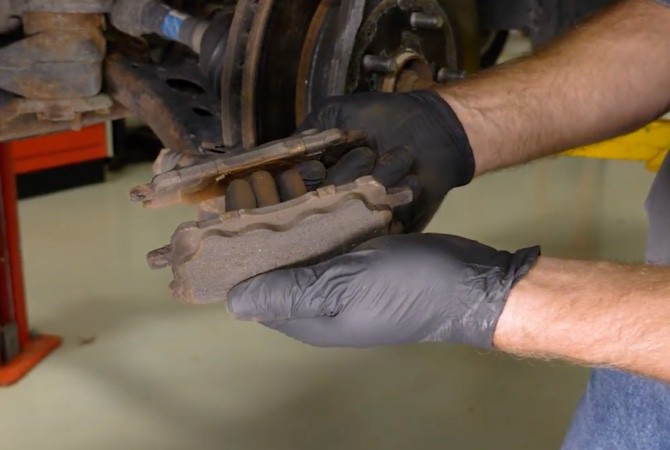 brake-system-inspection-part2-hero-step4-examine-brake-pads Technician examining brake pads in a brake system
